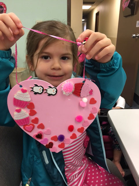 A child is holding up a pink tactile Valentine with shapes and hearts